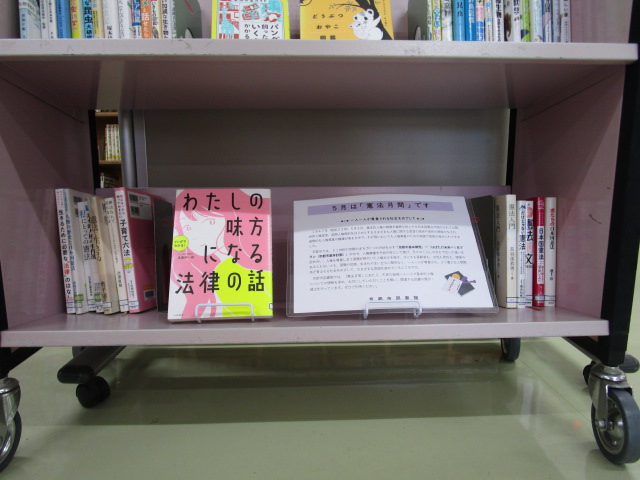 カートの上に本が並べられている写真。「5月は『憲法月間』です」というポスターを掲示しています。