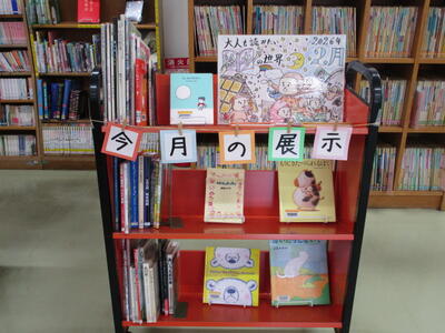 本を載せたカートの写真。「今月の展示」「大人も読みたい絵本の世界」という掲示がなされています。