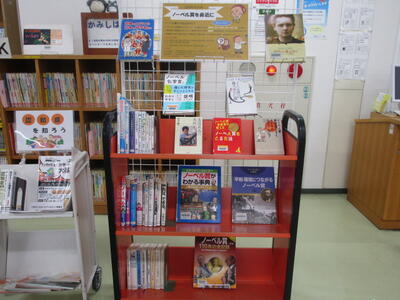 本を載せたカートの写真。「今月の展示」「ノーベル賞を身近に」と題された掲示がなされています。
